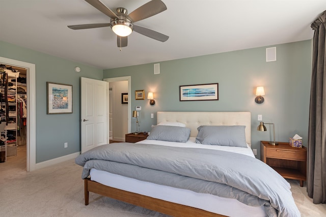bedroom featuring a walk in closet, light carpet, a closet, a ceiling fan, and baseboards