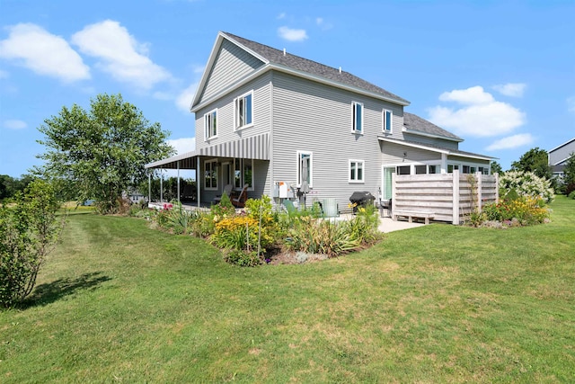 rear view of house featuring a patio area, a yard, and a shingled roof