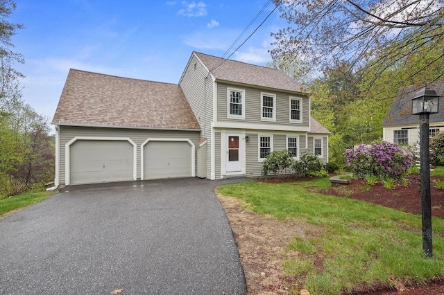 colonial-style house with a garage, a shingled roof, asphalt driveway, and a front lawn