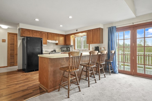 kitchen featuring freestanding refrigerator, under cabinet range hood, a peninsula, light countertops, and recessed lighting