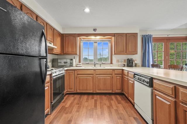 kitchen featuring freestanding refrigerator, electric range, dishwasher, under cabinet range hood, and light wood-style floors
