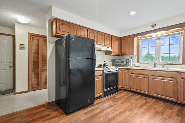 kitchen with black appliances, under cabinet range hood, light wood finished floors, light countertops, and brown cabinets