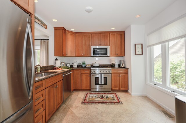 203 Straw Hill Rd, Manchester, NH 03104 - kitchen featuring stainless steel appliances, a sink, baseboards, brown cabinetry, and dark stone countertops