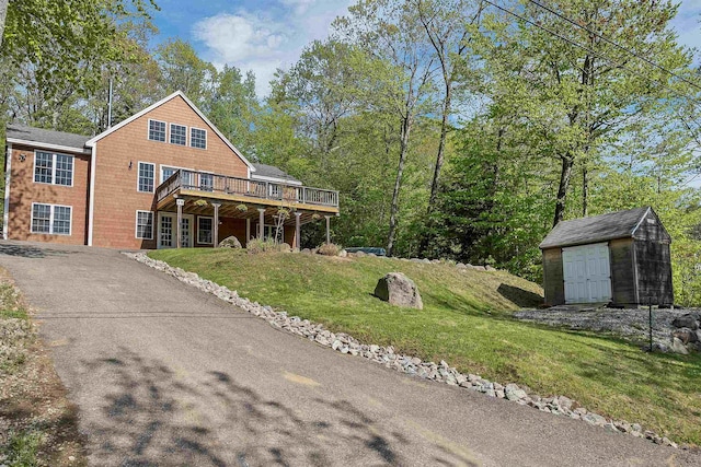 view of front of home featuring a shed, an outdoor structure, a deck, a front lawn, and asphalt driveway