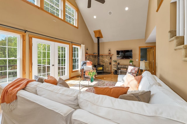 living room with high vaulted ceiling, a wood stove, wood finished floors, ceiling fan, and french doors