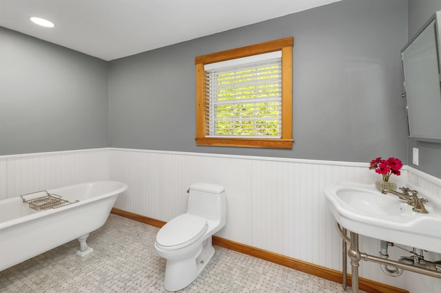 full bath featuring a wainscoted wall, a freestanding tub, toilet, and baseboards