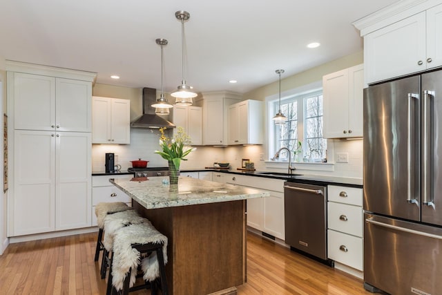 kitchen with appliances with stainless steel finishes, wall chimney exhaust hood, a kitchen island, light wood-type flooring, and a sink