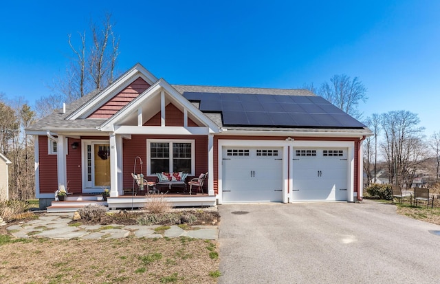 view of front of house with a garage, solar panels, asphalt driveway, covered porch, and a shingled roof