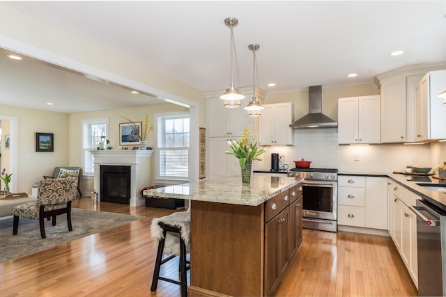 kitchen featuring appliances with stainless steel finishes, wall chimney range hood, light wood-type flooring, open floor plan, and a kitchen breakfast bar