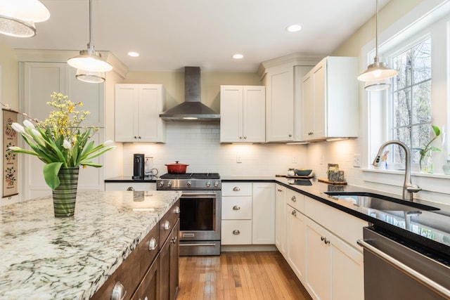 kitchen with appliances with stainless steel finishes, wall chimney range hood, a sink, light stone countertops, and hardwood / wood-style flooring