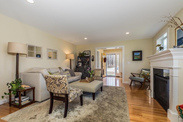 living room with light wood-style flooring, a glass covered fireplace, recessed lighting, and baseboards