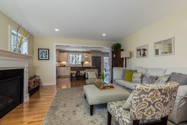 living room featuring light wood-style flooring, healthy amount of natural light, recessed lighting, a glass covered fireplace, and baseboards