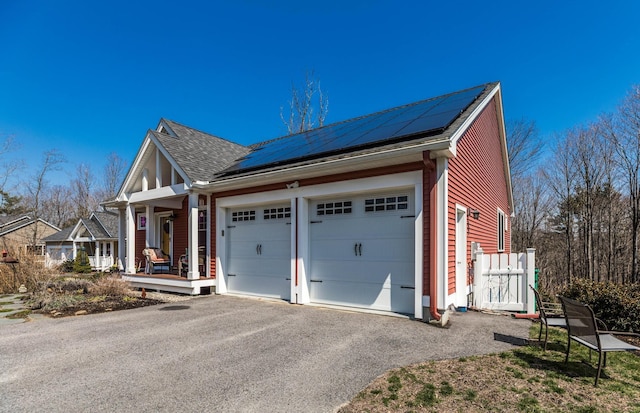 view of front facade with roof mounted solar panels, an attached garage, driveway, a porch, and roof with shingles