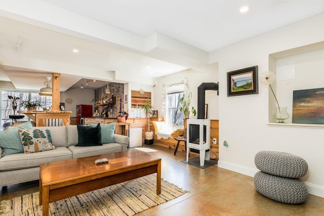 living area featuring a wood stove, baseboards, recessed lighting, and concrete flooring