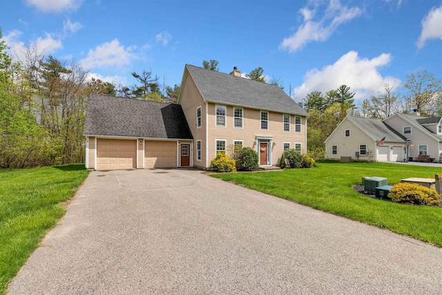 colonial home with an attached garage, a chimney, driveway, a front yard, and central AC