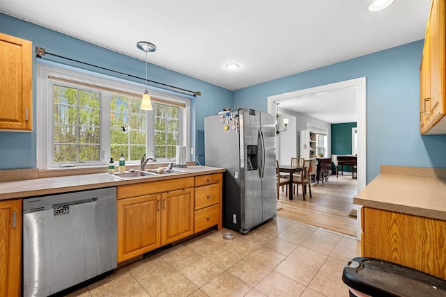 kitchen with appliances with stainless steel finishes, a sink, light countertops, light tile patterned floors, and decorative light fixtures