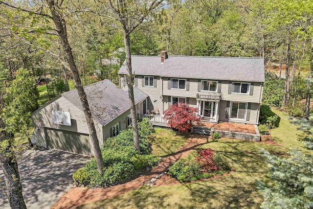 view of front facade with a chimney, a garage, concrete driveway, a wooded view, and roof with shingles