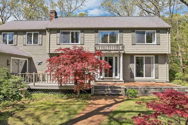 rear view of house with a chimney, a lawn, roof with shingles, and a deck