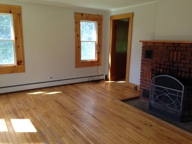 1413 Main St, Pittsburg, NH 03592 - unfurnished living room featuring crown molding, wood finished floors, baseboard heating, and a brick fireplace