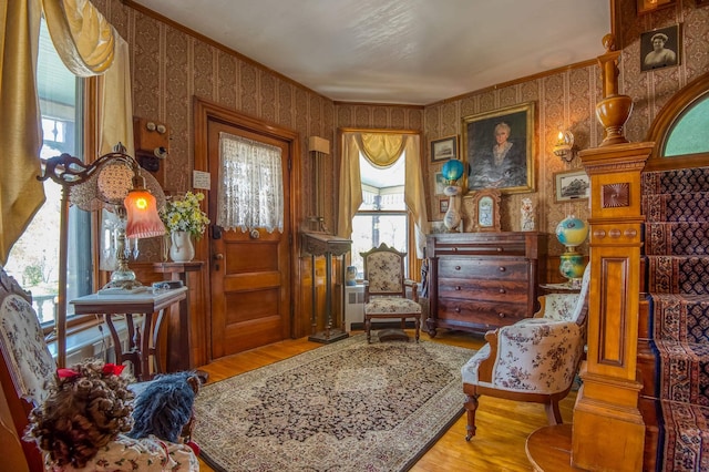 living area with wallpapered walls, wood finished floors, healthy amount of natural light, and crown molding