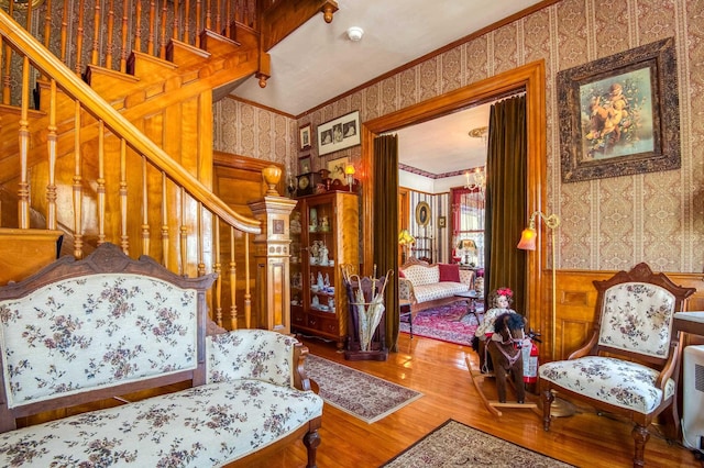 living room with wallpapered walls, crown molding, wood finished floors, and stairway