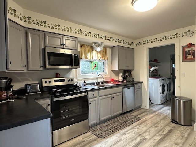 kitchen with appliances with stainless steel finishes, separate washer and dryer, dark countertops, a sink, and gray cabinetry