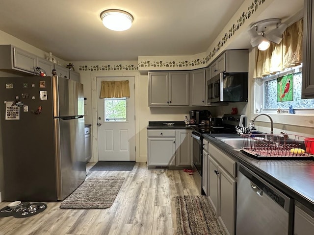 kitchen featuring appliances with stainless steel finishes, a sink, dark countertops, gray cabinets, and light wood-style flooring