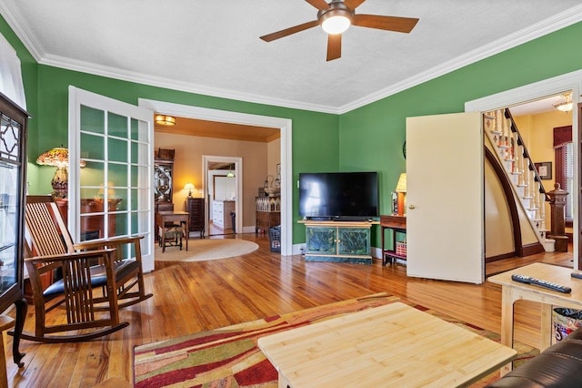 living area featuring wood-type flooring, a ceiling fan, stairway, ornamental molding, and baseboards