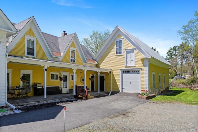 view of front of property with a porch, asphalt driveway, a garage, and a chimney