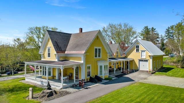 view of front of house with covered porch, driveway, a front lawn, and a chimney