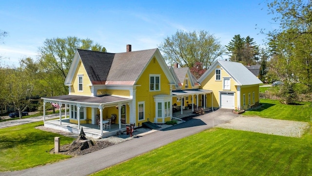 view of front of property with covered porch, a front lawn, a chimney, and driveway