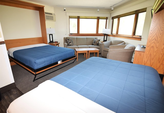 bedroom featuring wood finished floors, track lighting, and an AC wall unit