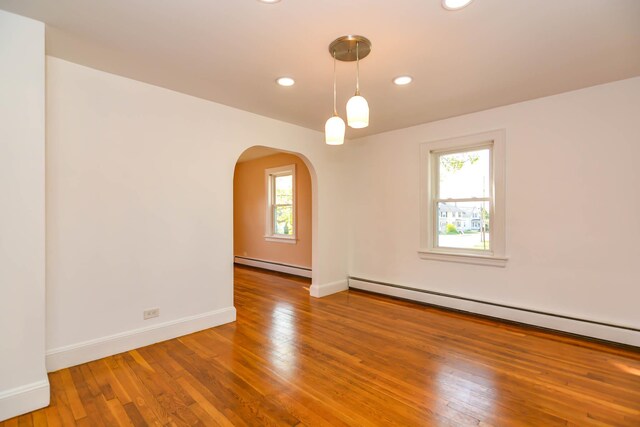 unfurnished room featuring a baseboard heating unit, arched walkways, recessed lighting, baseboards, and wood finished floors