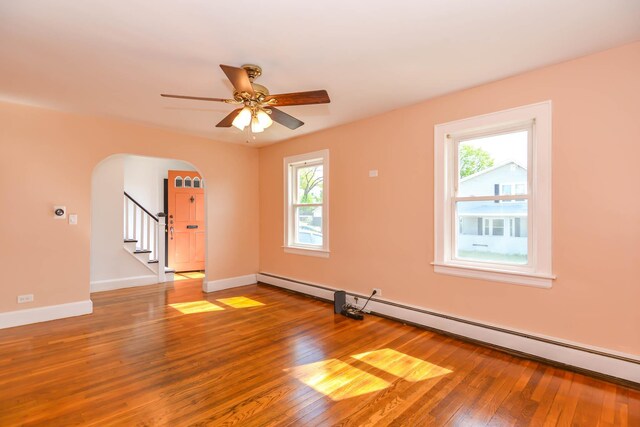 unfurnished room featuring arched walkways, plenty of natural light, hardwood / wood-style floors, and a baseboard radiator