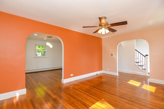 empty room featuring arched walkways, a baseboard radiator, ceiling fan, wood finished floors, and baseboards