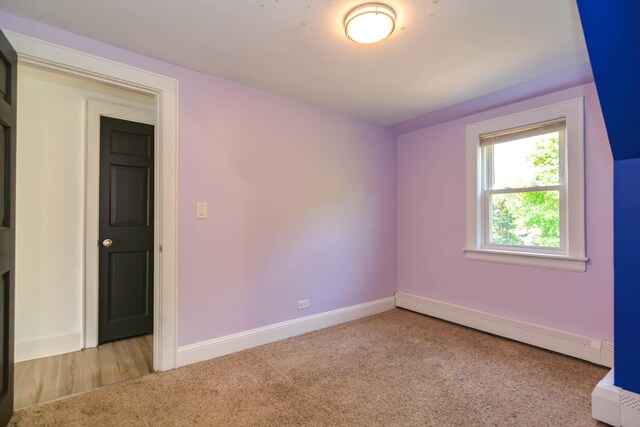 carpeted empty room featuring a baseboard heating unit and baseboards