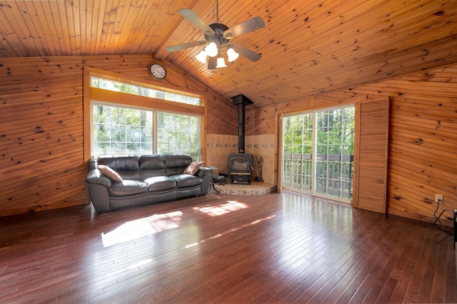 living room featuring wooden walls, vaulted ceiling, a wood stove, a ceiling fan, and hardwood / wood-style floors