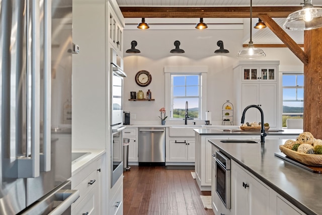kitchen with stainless steel appliances, a sink, beam ceiling, white cabinetry, and hanging light fixtures
