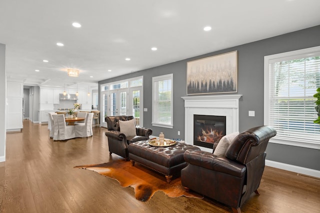 living room featuring recessed lighting, a glass covered fireplace, plenty of natural light, wood finished floors, and baseboards