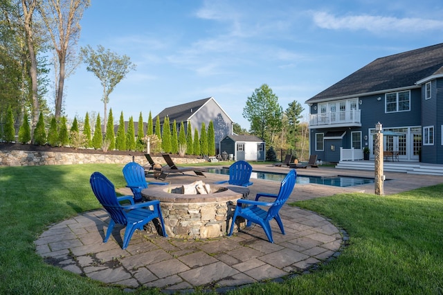 view of patio / terrace with an outdoor fire pit, a storage shed, an outdoor structure, an outdoor pool, and a balcony