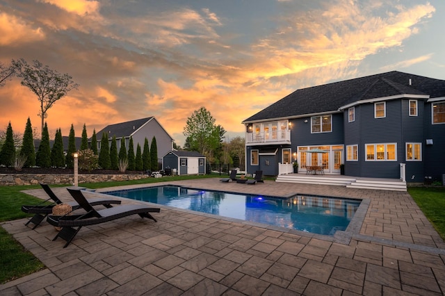 swimming pool with a storage shed, an outdoor structure, and a patio area