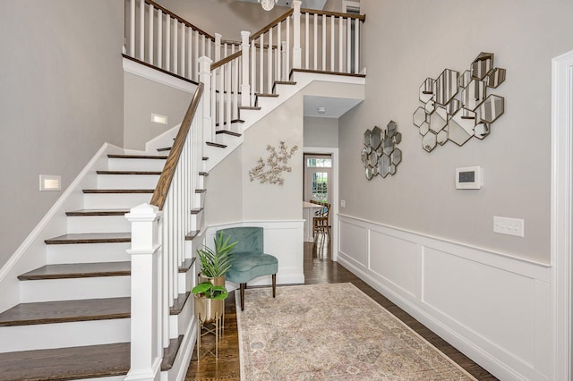 staircase with wood finished floors, a towering ceiling, and a wainscoted wall