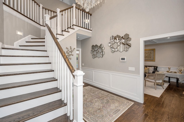 stairs with a towering ceiling, wood finished floors, a wainscoted wall, a decorative wall, and a chandelier