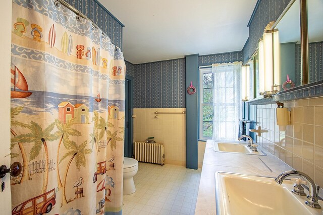 685 Abbot Hill Rd, Wilton, NH 03086 - bathroom featuring radiator, wallpapered walls, a sink, tile walls, and a wainscoted wall