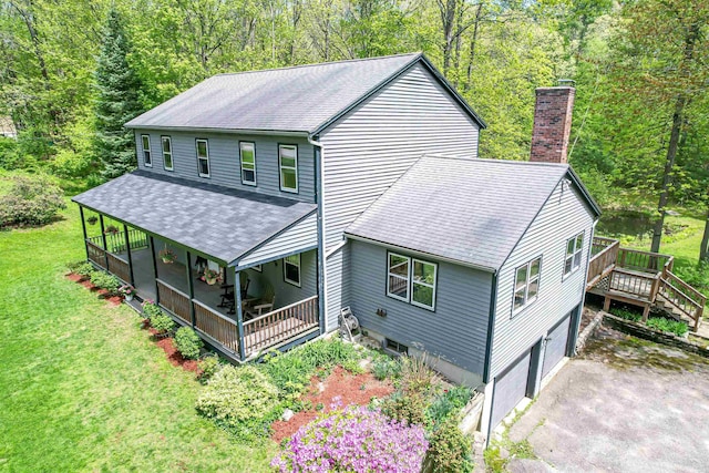 rear view of house with a chimney, roof with shingles, asphalt driveway, a lawn, and an attached garage