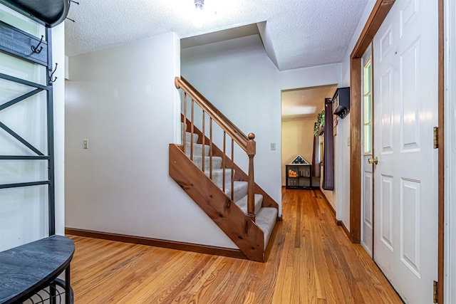 foyer featuring light wood finished floors, a textured ceiling, stairway, and baseboards