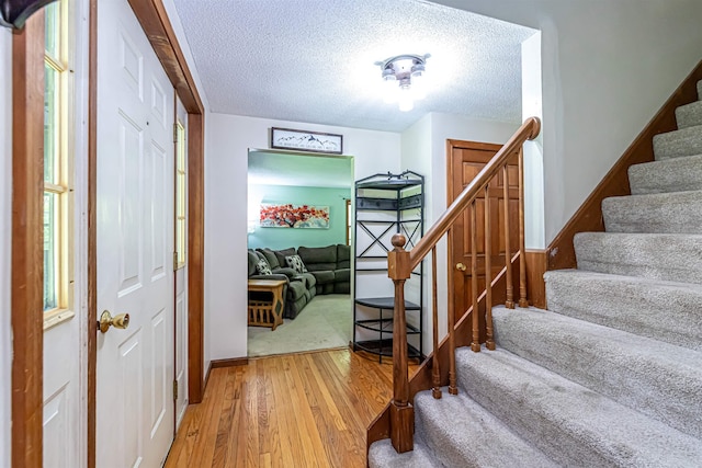 foyer with light wood-type flooring, stairs, a textured ceiling, and baseboards