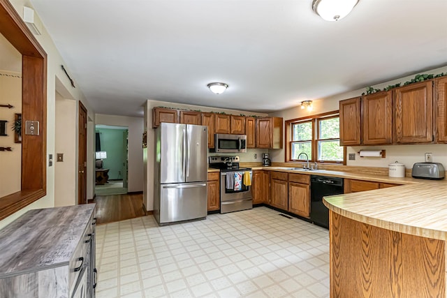 kitchen featuring appliances with stainless steel finishes, a sink, brown cabinetry, light countertops, and light flooring