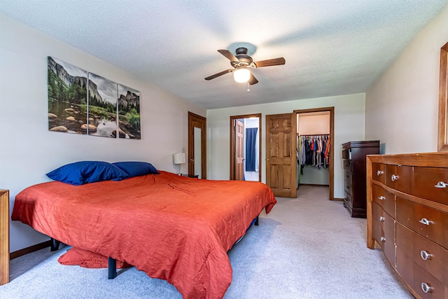 bedroom featuring a walk in closet, light carpet, a closet, a textured ceiling, and ceiling fan
