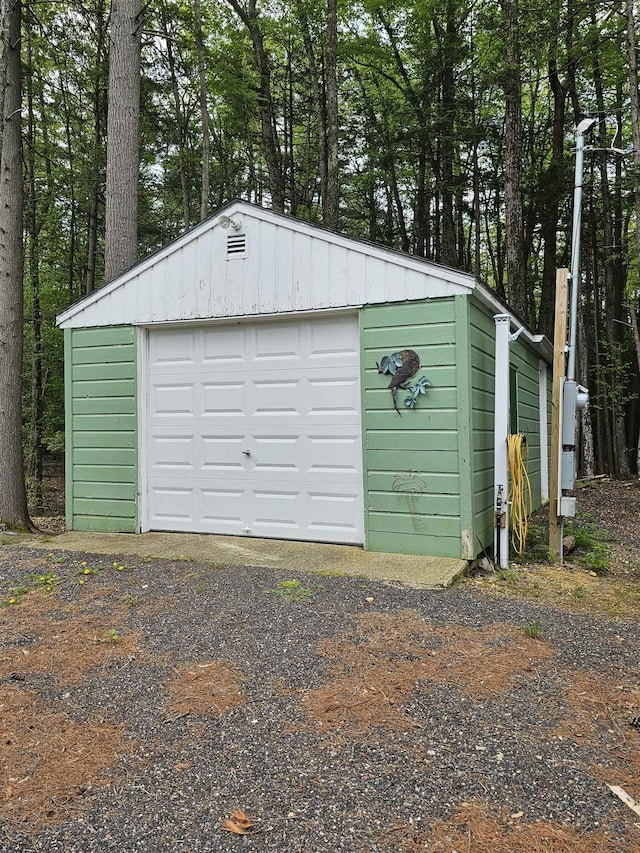 detached garage featuring dirt driveway and view of scattered trees